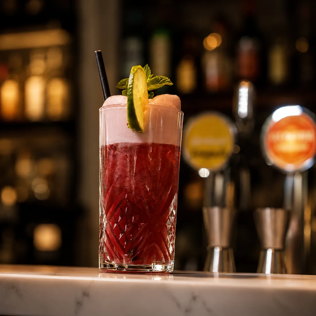 Cocktail rouge à la mousse rosée devant les tireuses du bar