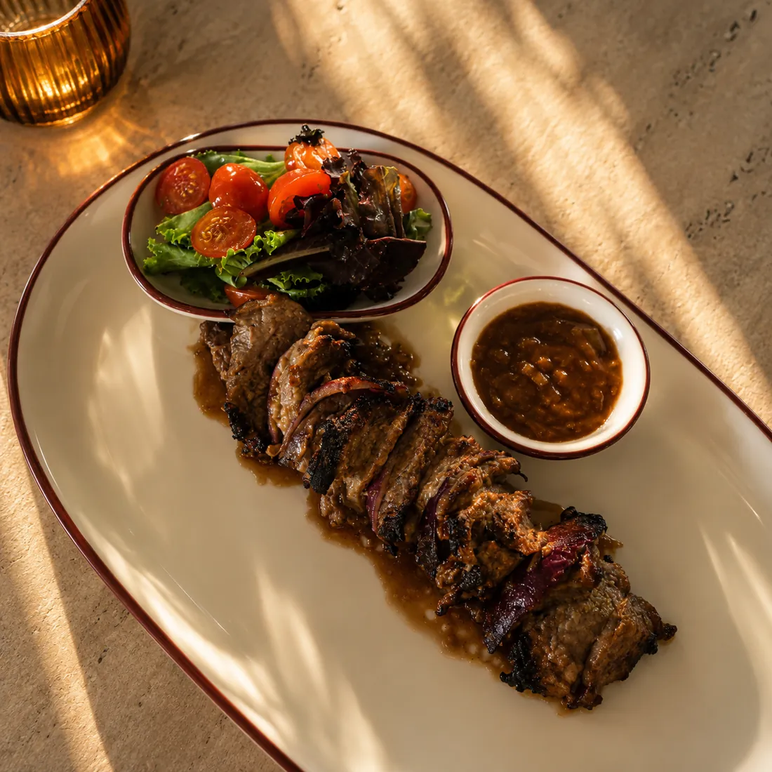 Bœuf grillé tranché sur plat ovale avec sauce et salade