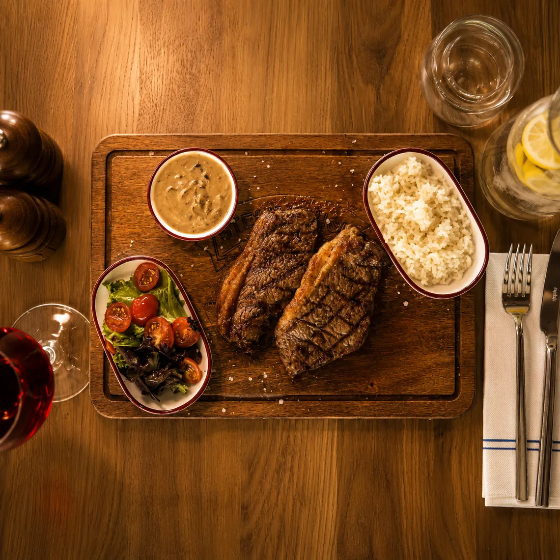 Deux pièces de bœuf grillées sur planche avec sauce, riz et salade