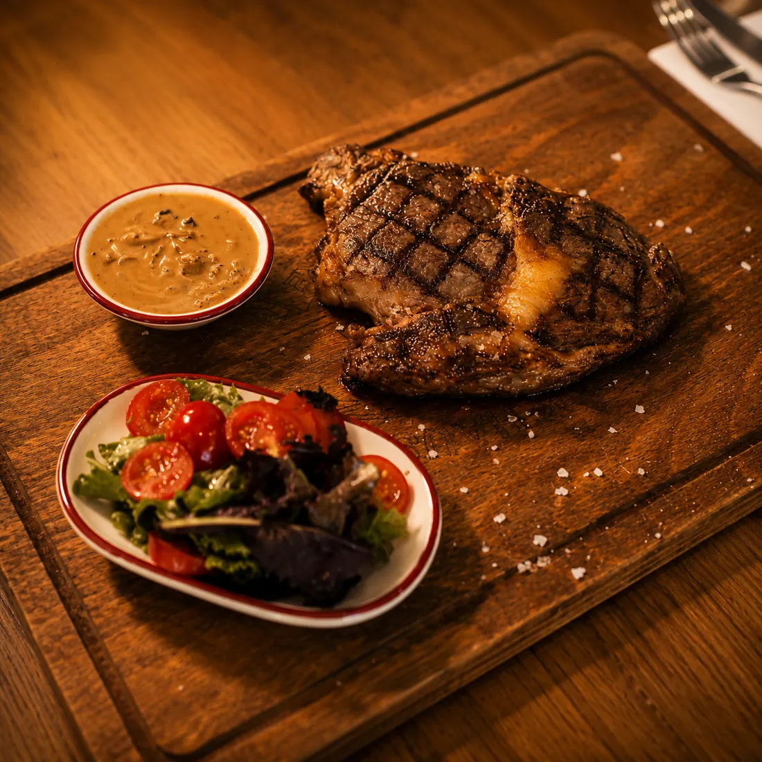 Entrecôte grillée sur planche en bois avec sauce et salade